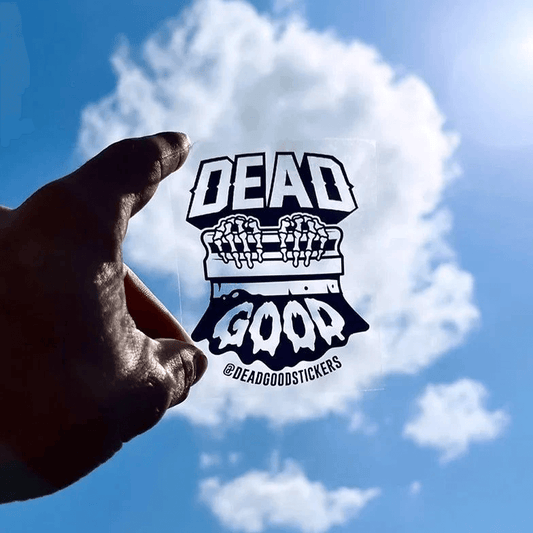 Hand holding a DeadGood transparent vinyl sticker against the sky, showing clear background effect