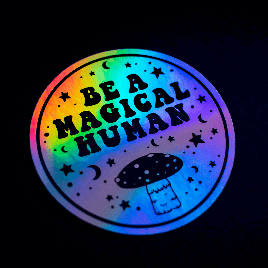 Round, multi-coloured holographic sticker with 'Be a Magical Human' text and mushroom graphic on a black background.